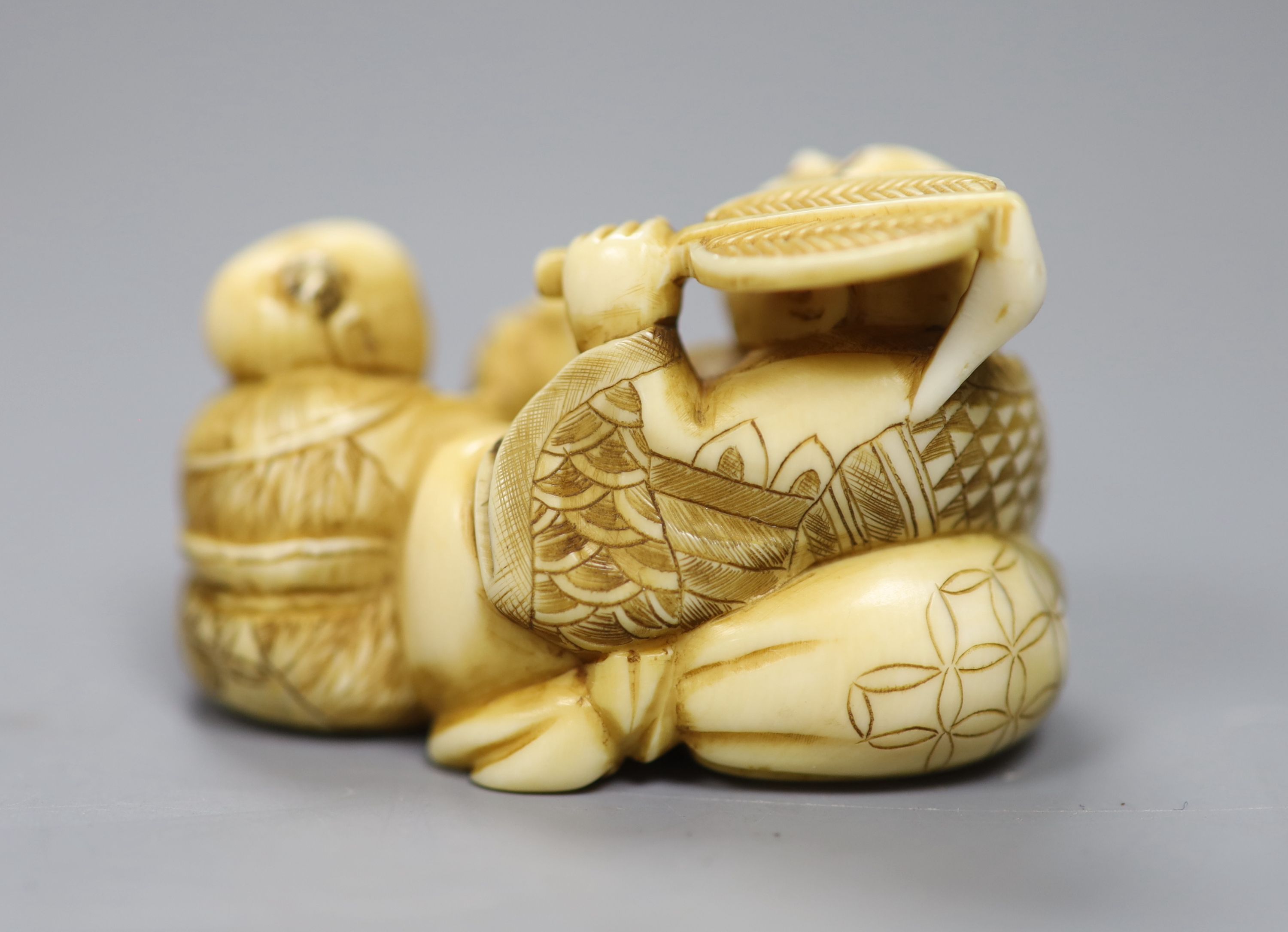 A Japanese ivory netsuke in the form of a seated Hotei and attendant, early 20th century 3cm high, 5cm wide, signed to underside, toget